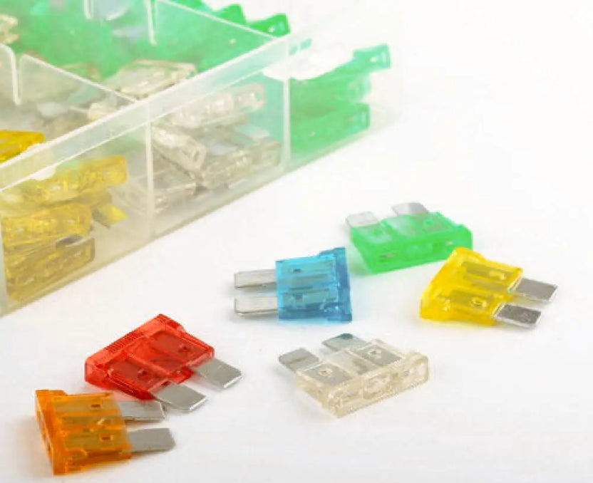 Assorted colored fuses on a white surface with a clear plastic container.