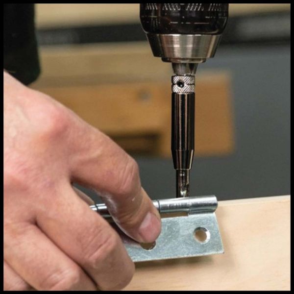 A close-up of a hand using a drill to fasten a silver metal bracket onto a light wood surface.