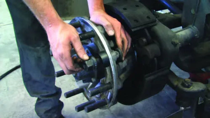 Person working on a mechanical component, possibly a brake system, with a focus on hands and machinery.