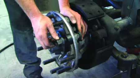 Person working on a mechanical component, possibly a brake system, with a focus on hands and machinery.