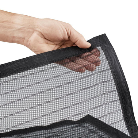 A close-up of a hand holding the corner of a black mesh screen or filter panel with a black stitched border, shown against a plain white background.
