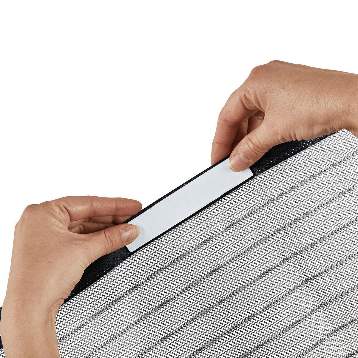 Close-up of a person's hands applying a white adhesive strip to the edge of a gray and black striped mesh panel, set against a plain white background.