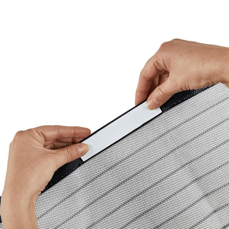 Close-up of a person's hands applying a white adhesive strip to the edge of a gray and black striped mesh panel, set against a plain white background.