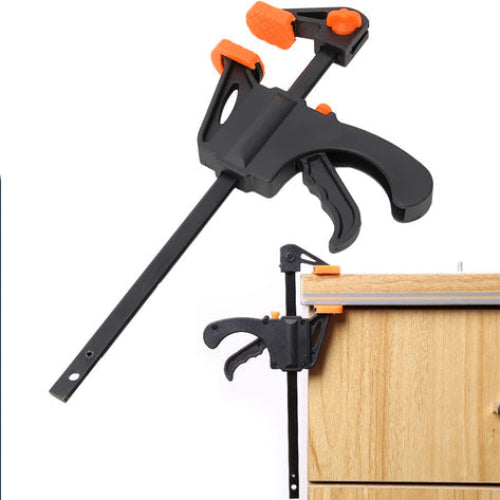 Black and orange clamping tool attached to a wooden surface on a white background