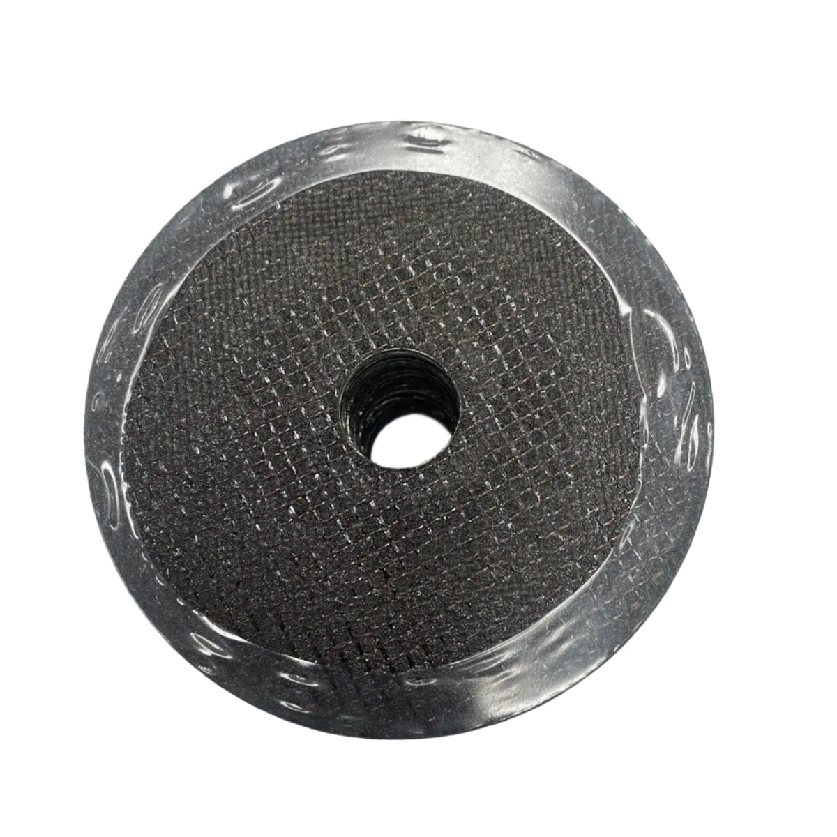 A circular metallic mesh filter or strainer with a central hole, resting on a white sheet of paper over a dark wood surface.