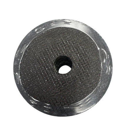 A circular metallic mesh filter or strainer with a central hole, resting on a white sheet of paper over a dark wood surface.