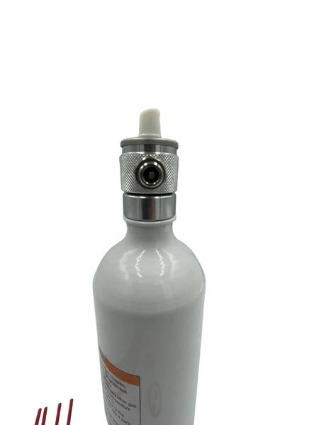 A white ceramic bottle with a silver metal collar and a white plastic cap, shown against a white studio background with a softbox visible on the right.