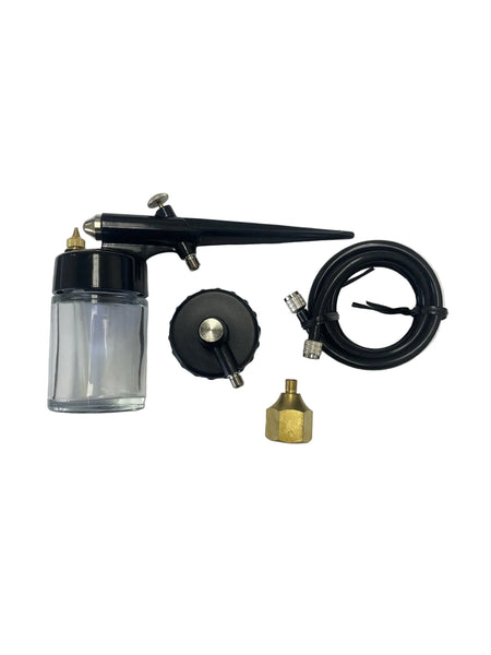An airbrush kit laid out on a white surface, including a clear plastic oil bottle with a black cap, a black airbrush pen, a black hose with metal connectors, a round black cap, and a small brass fitting.